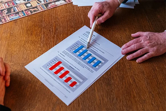 Hand zeigt mit Kugelschreiber auf Dokument mit Auswertungen und Balkendiagrammen