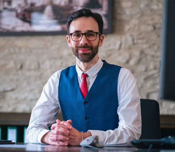 Portrait eines Steuerberaters im blauen Anzug mit roter Krawatte am Schreibtisch vor Steinwand